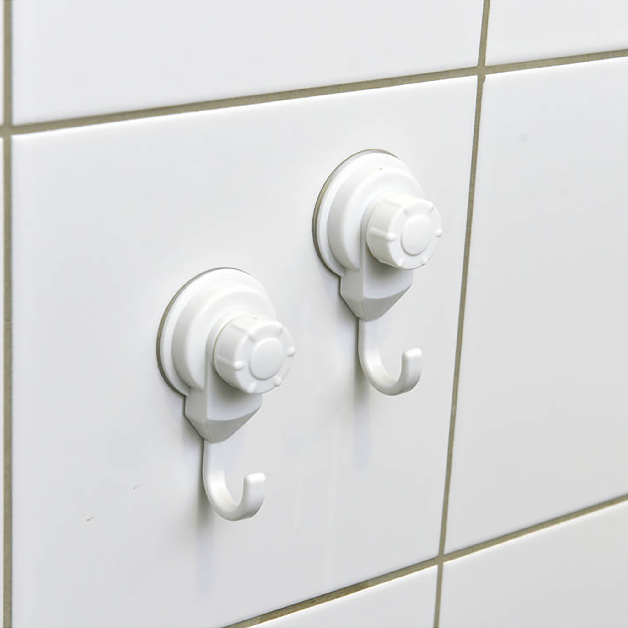 Two white suction cup hooks mounted on white ceramic tiles, close-up view