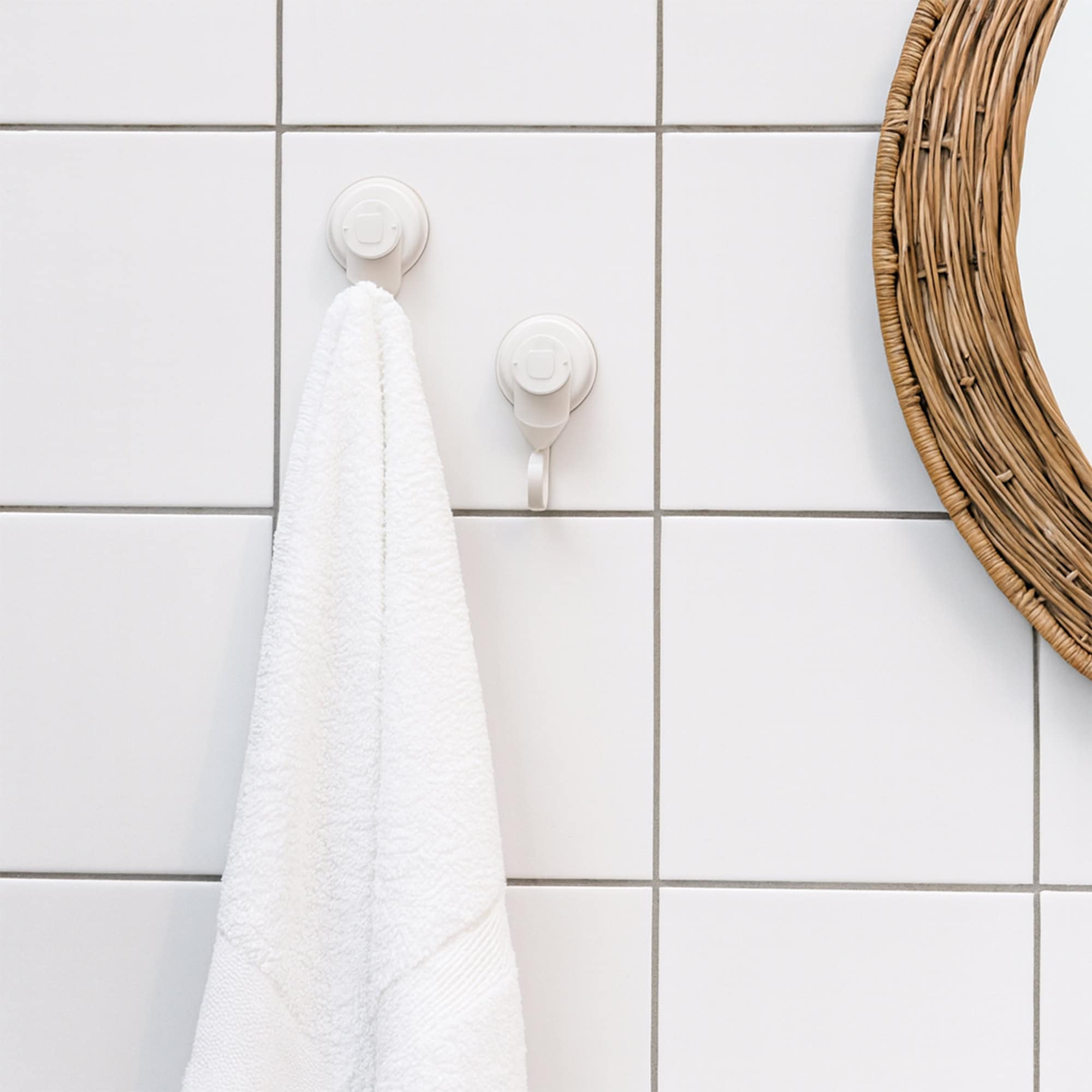 Two white suction cup hooks on tiled wall, one holding a white towel