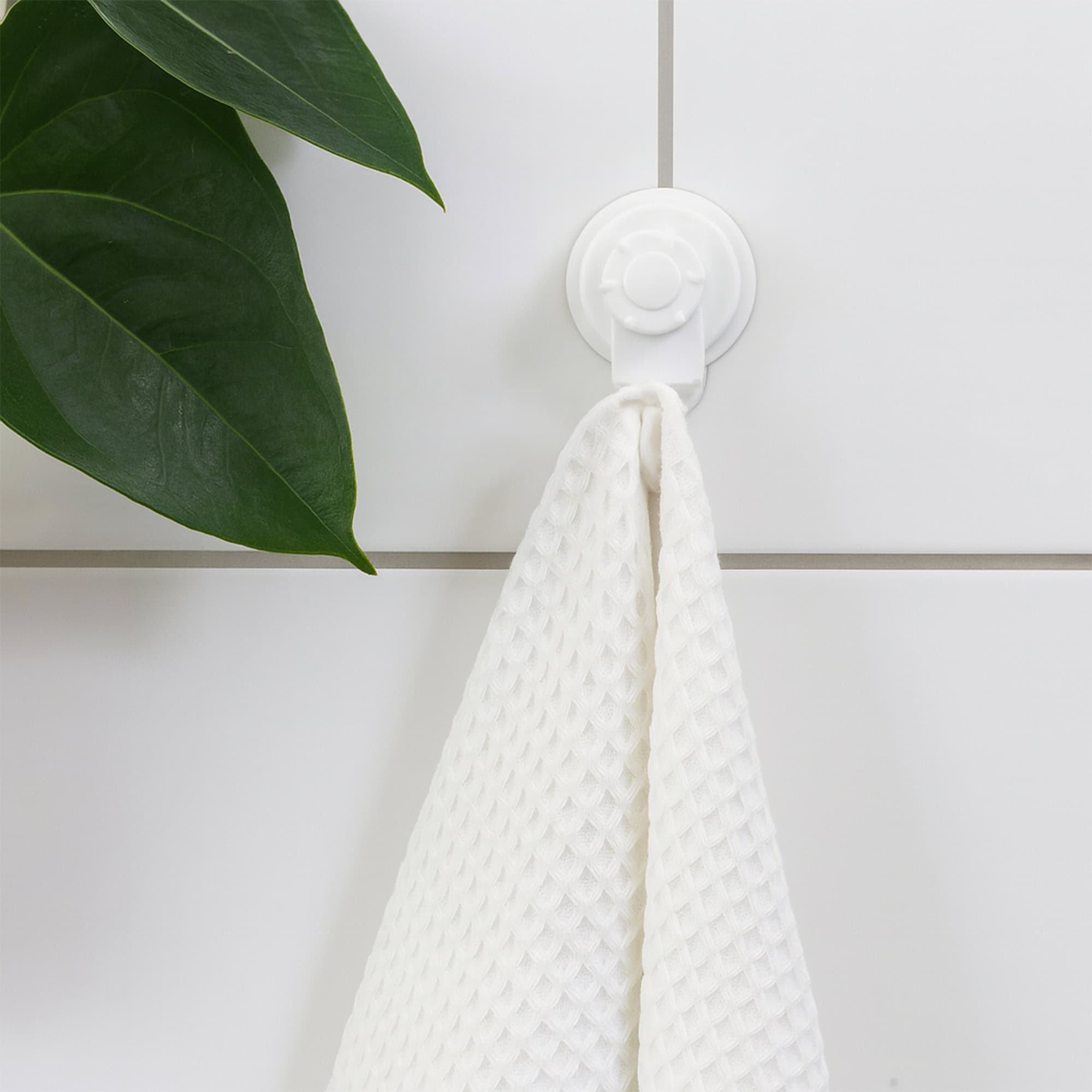Single white suction cup hook on large-format white tiles holding a waffle-weave towel