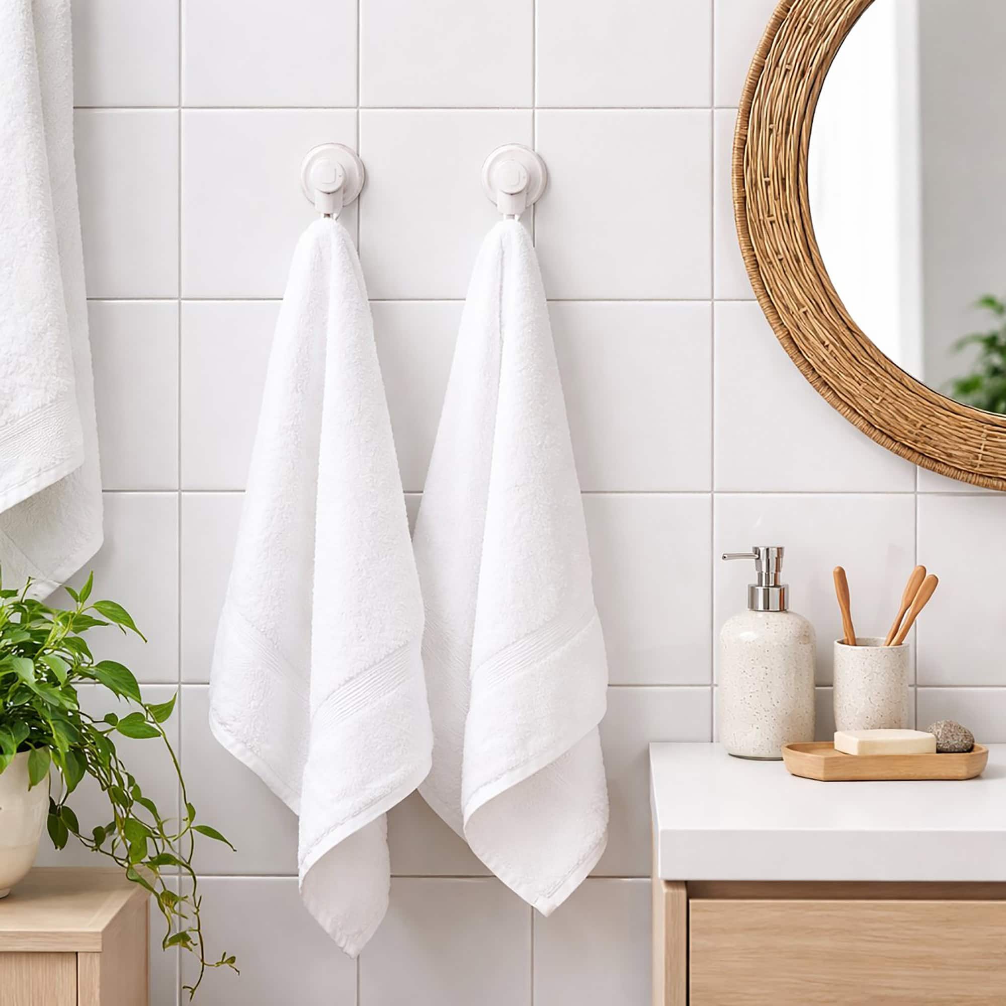 Two white suction cup hooks holding white towels on a tiled bathroom wall