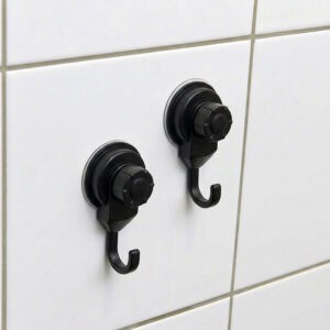 Two black suction cup hooks mounted on white ceramic tiles, close-up view