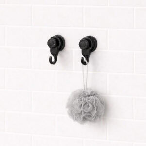 Two black suction cup hooks on white subway tiles holding a gray bath loofah