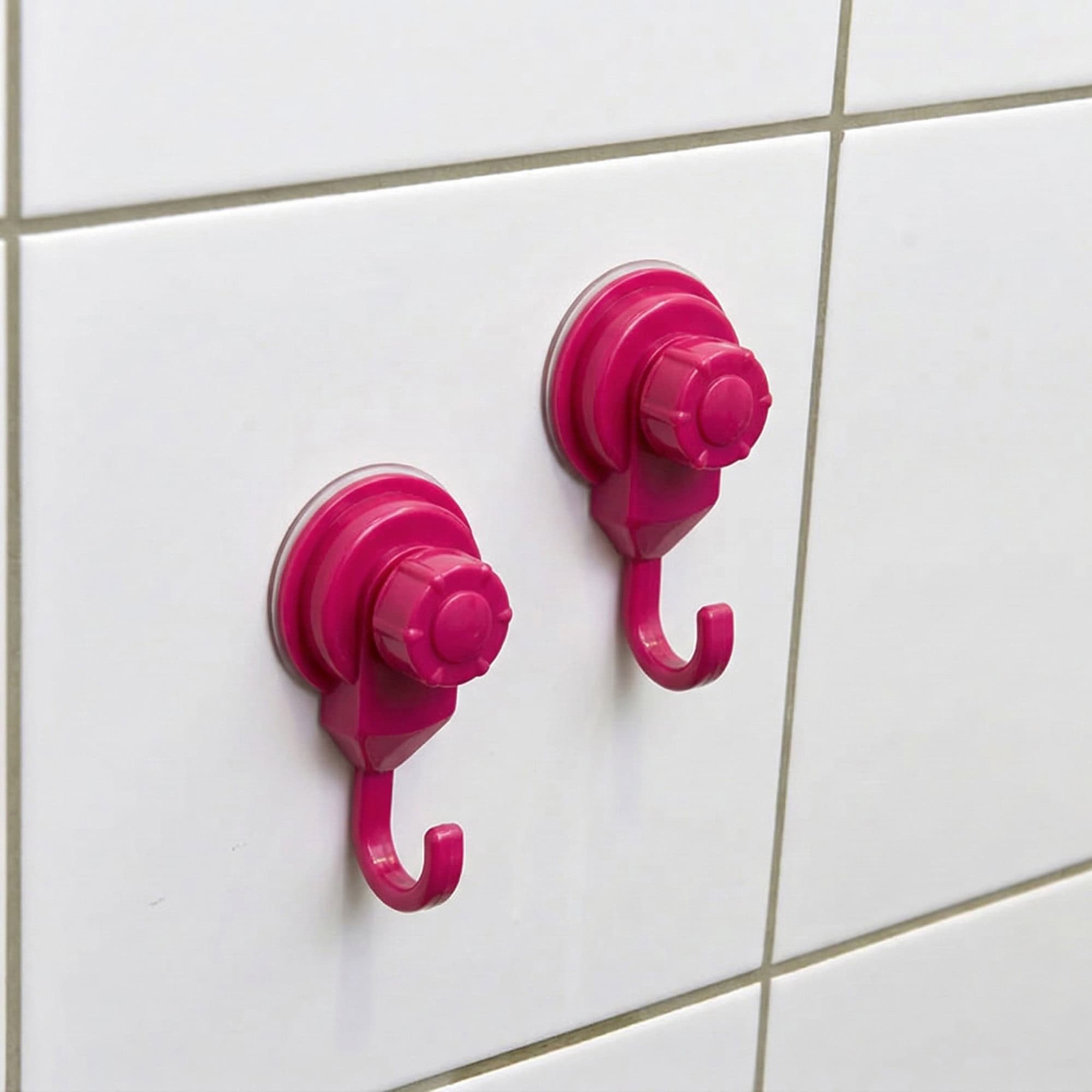Two hot pink suction cup hooks mounted on white ceramic tiles, close-up view