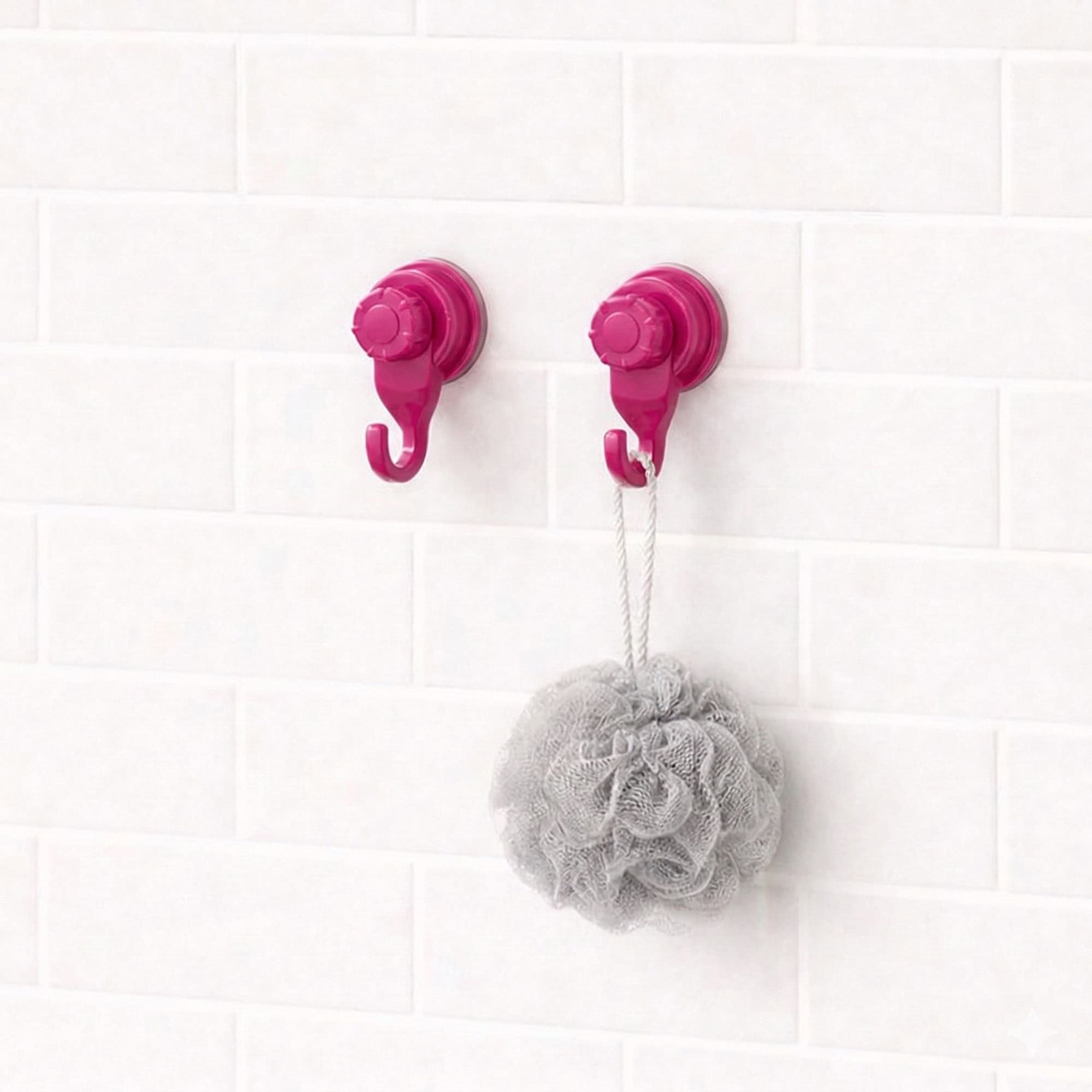 Two hot pink suction cup hooks on white subway tiles holding a gray bath loofah