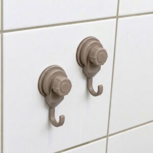 Two tan suction cup hooks mounted on white ceramic tiles, close-up view