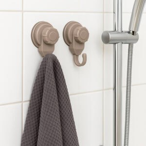 Two tan suction cup hooks on shower tiles holding a gray waffle-weave towel, with chrome shower rail visible