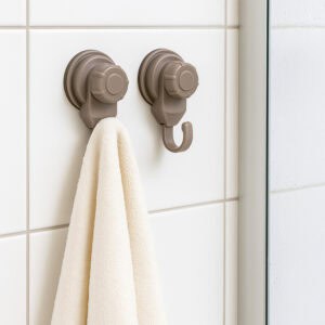 Two tan suction cup hooks on white tiles near a shower, one holding a cream towel
