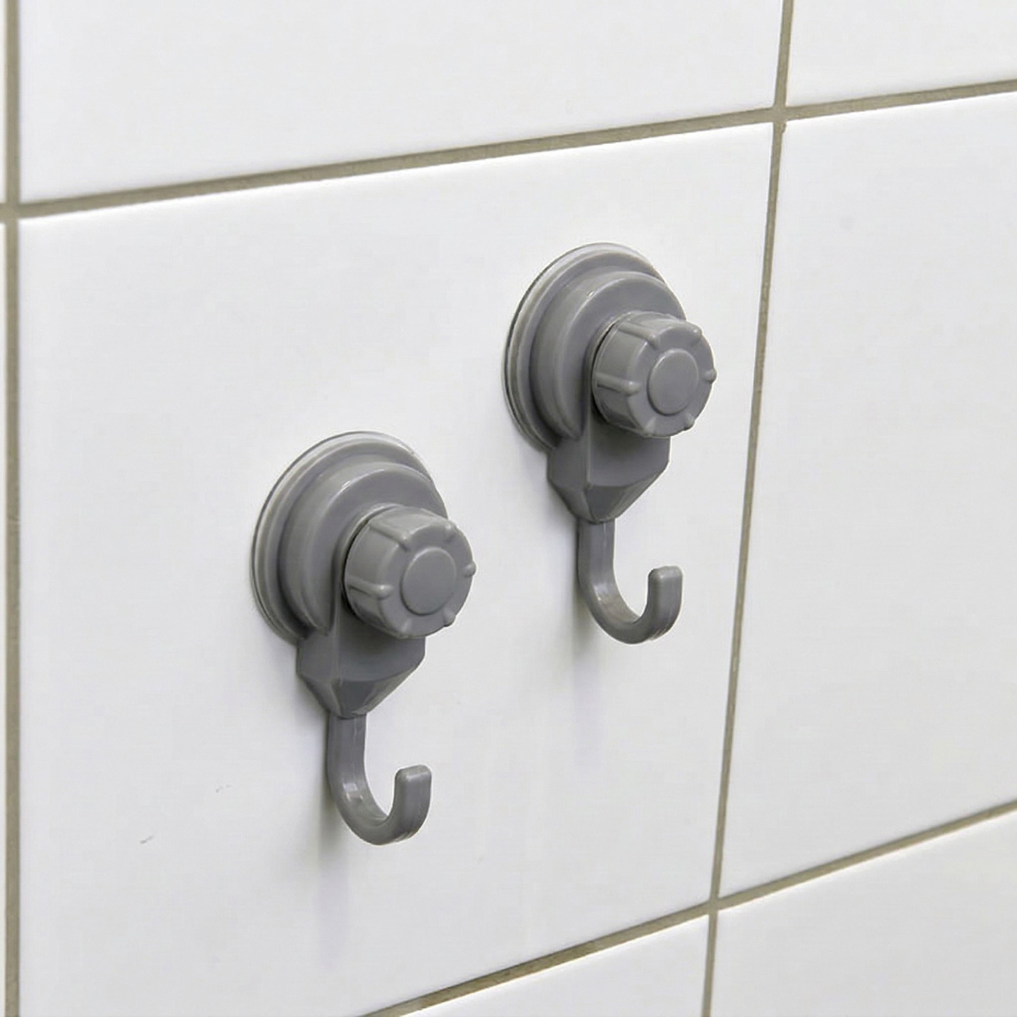 Two gray suction cup hooks mounted on white ceramic tiles, close-up view