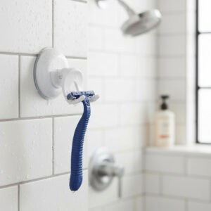 White suction cup razor holder on wet subway tile shower wall holding a blue razor, with showerhead in background