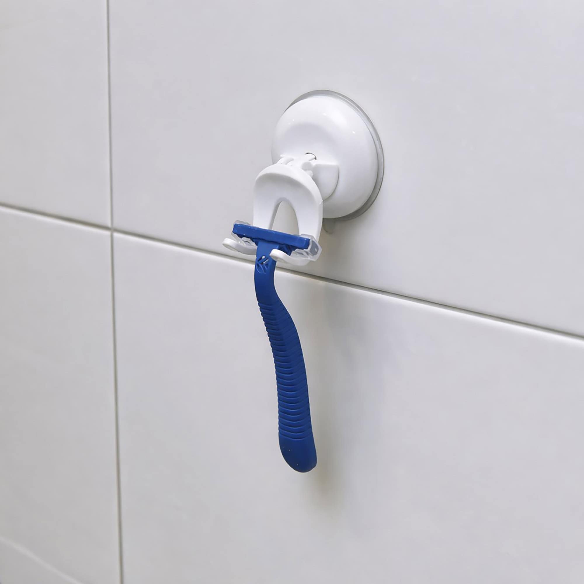 White suction cup razor holder on white tiles holding a blue disposable razor, close-up view