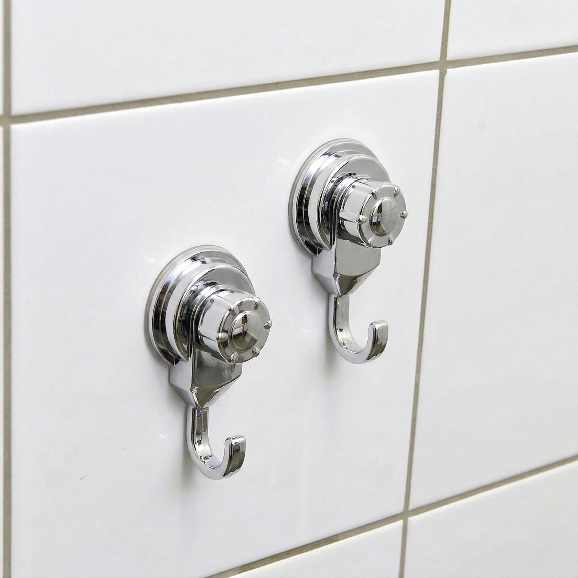 Two chrome suction cup hooks mounted on white ceramic tiles, close-up view