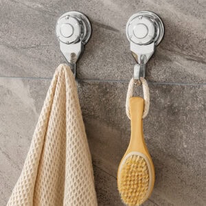 Two chrome suction cup hooks on gray stone tiles holding a cream waffle towel and wooden body brush