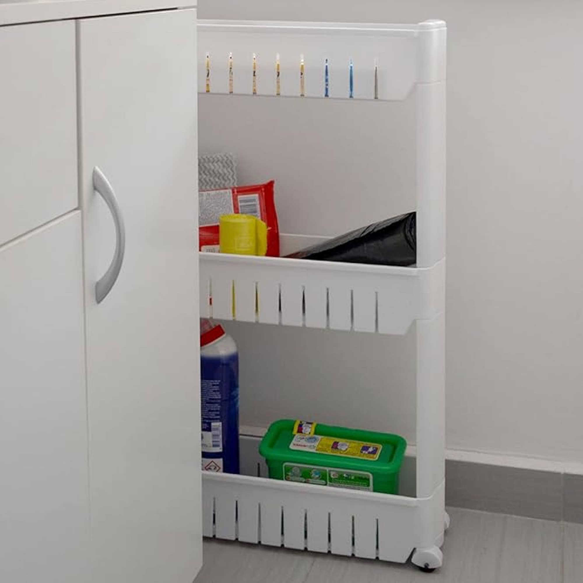 Narrow white 3-tier rolling organizer pulled out from between kitchen cabinets, holding cleaning supplies