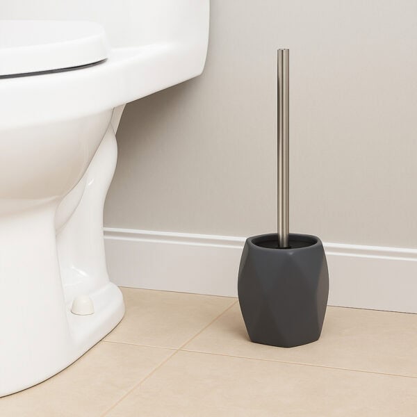 Gray diamond-shaped stoneware toilet brush holder with stainless steel handle beside white toilet