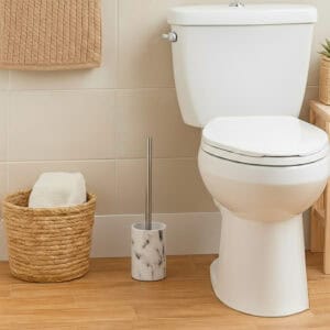 White marble effect toilet brush with stainless steel handle beside white toilet with woven basket on wood floor