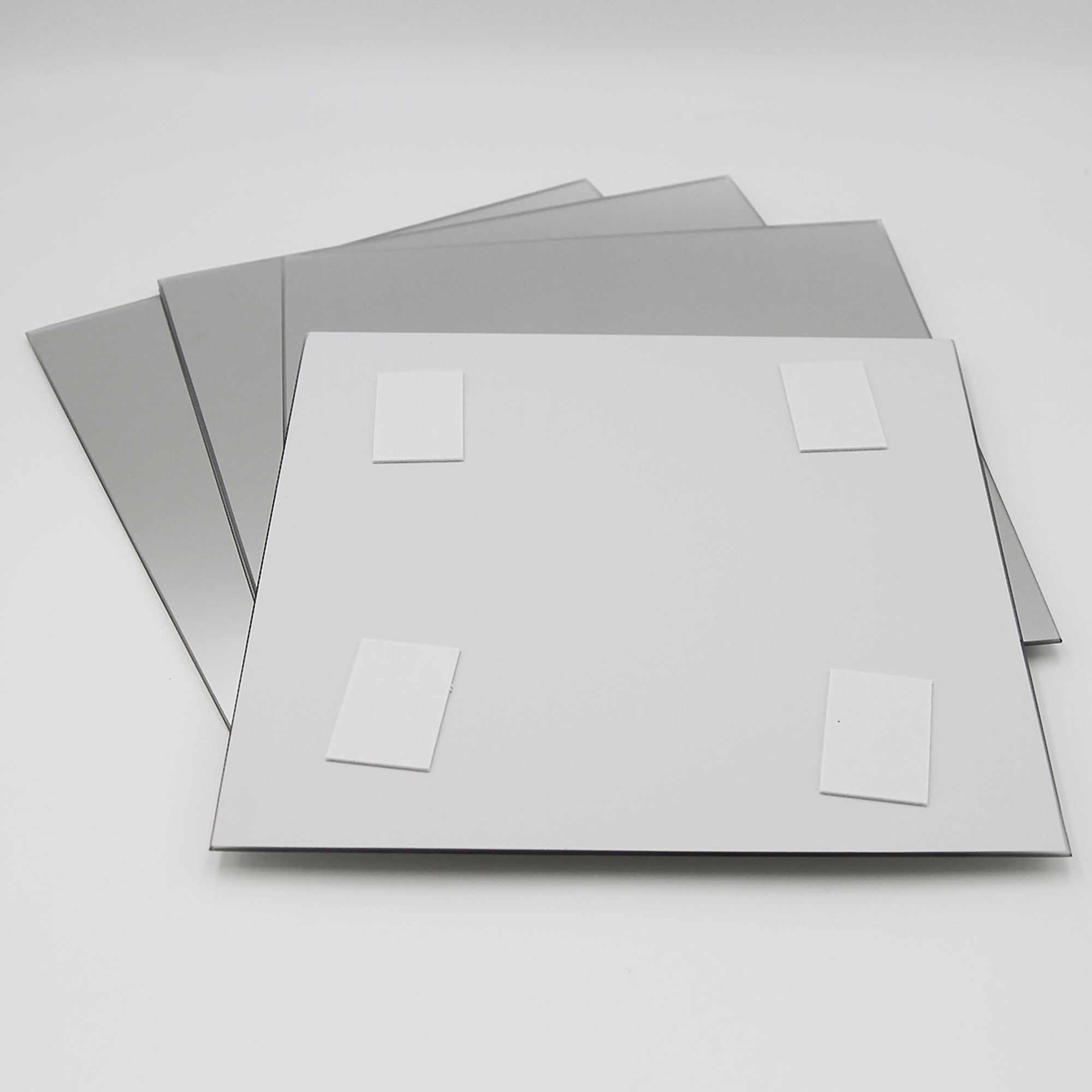 "Back of square mirror showing four adhesive foam mounting pads, with three additional mirrors stacked behind"