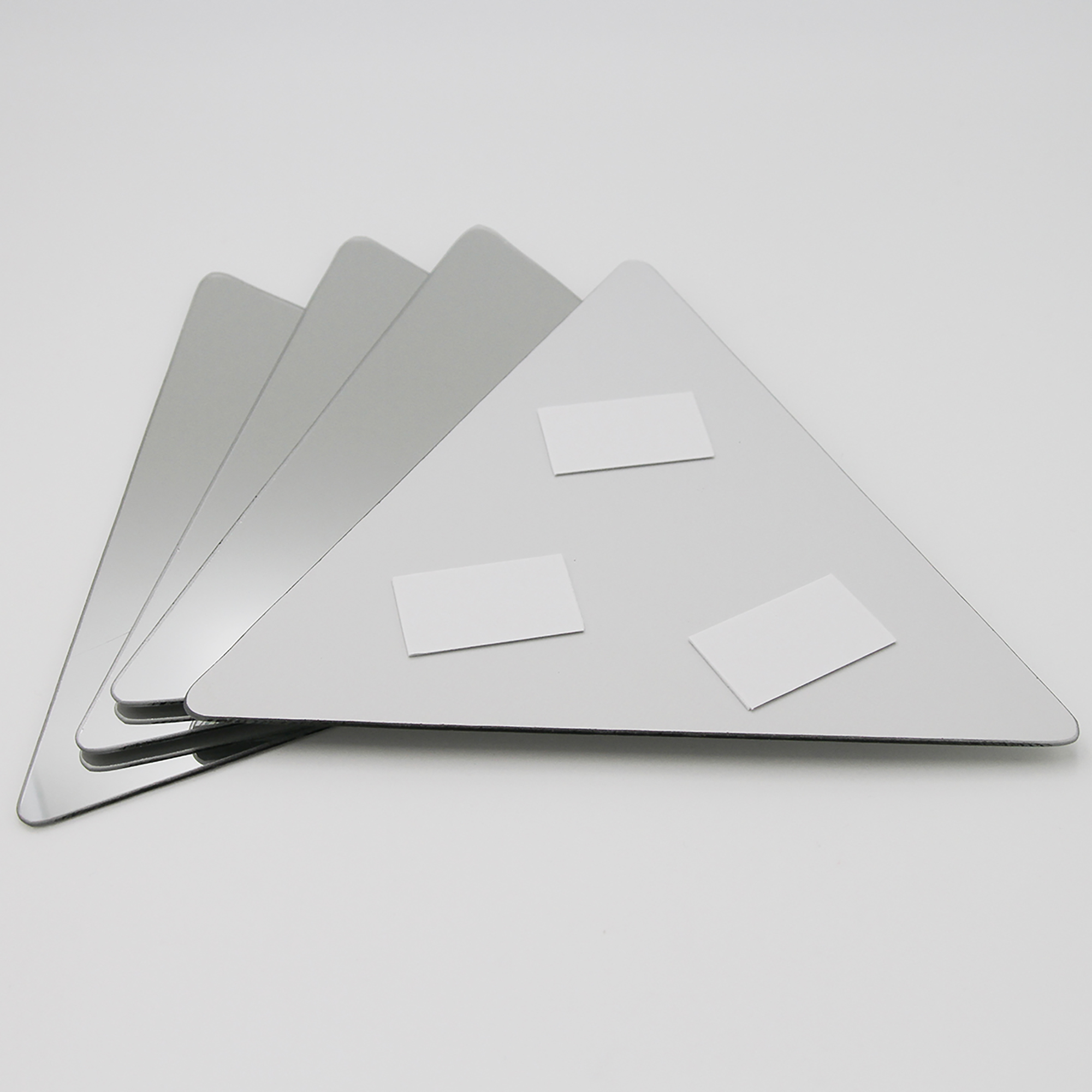 "Back of triangle mirror showing three adhesive foam mounting pads, with three additional mirrors fanned behind"