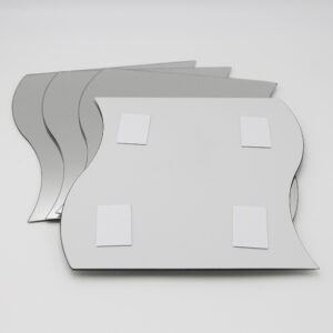 "Back of wave-shaped mirror showing four adhesive foam mounting pads, with three additional mirrors stacked behind"