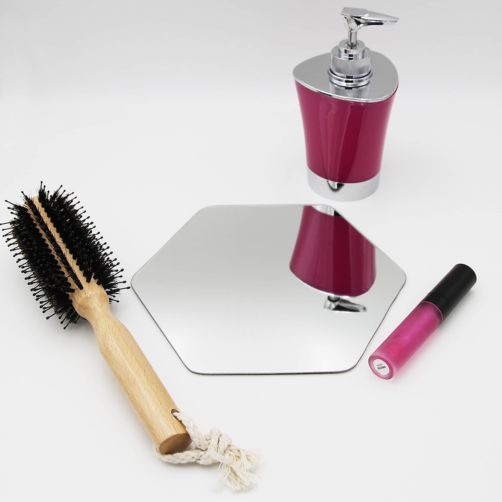 "Single hexagonal frameless mirror lying flat beside a hairbrush and cosmetics"