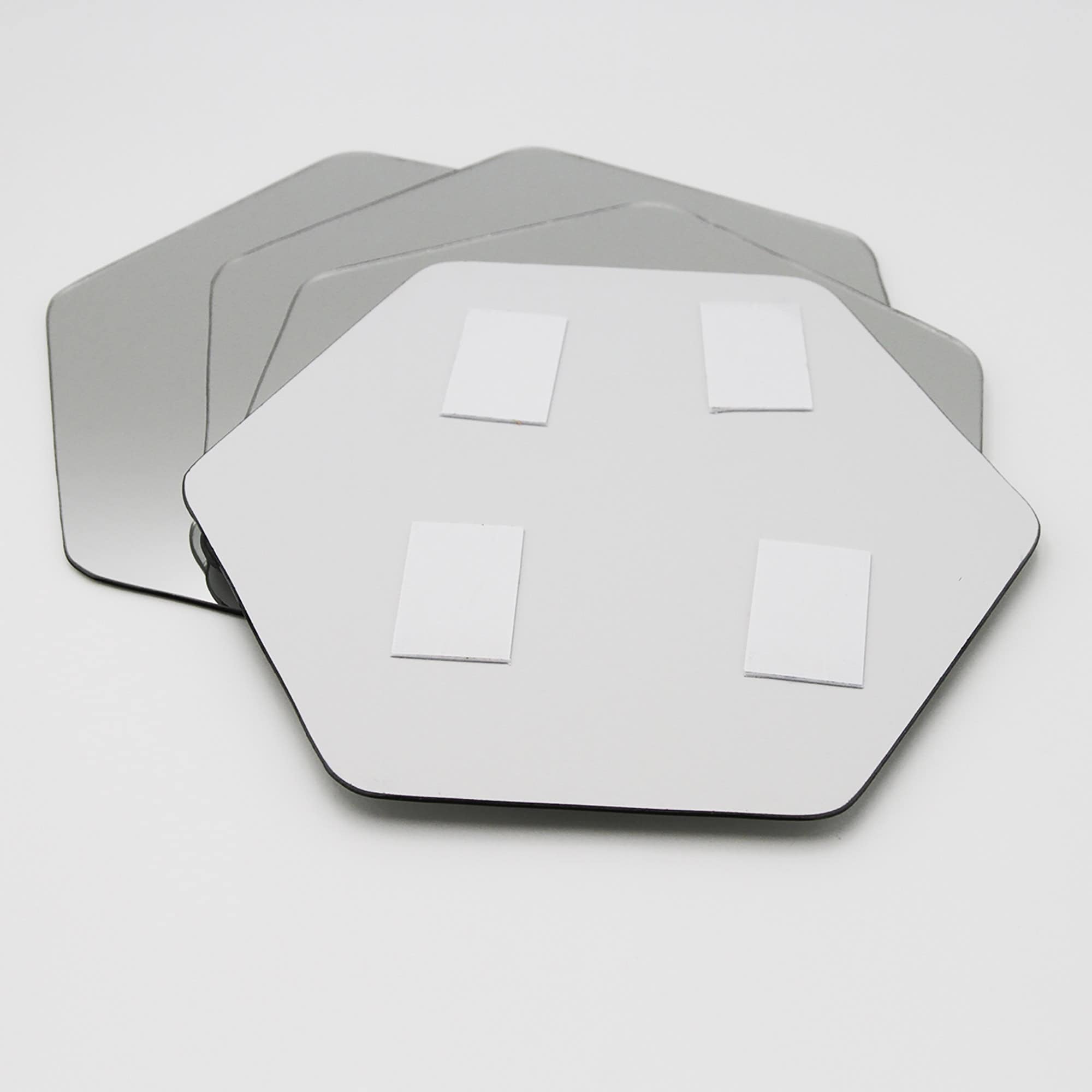 "Back of hexagonal mirror showing four adhesive foam mounting pads, with three additional mirrors stacked behind"