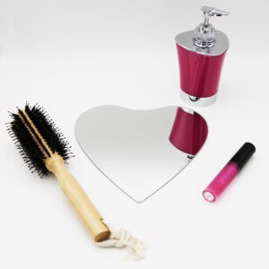 "Single heart-shaped frameless mirror lying flat beside a hairbrush and cosmetics"