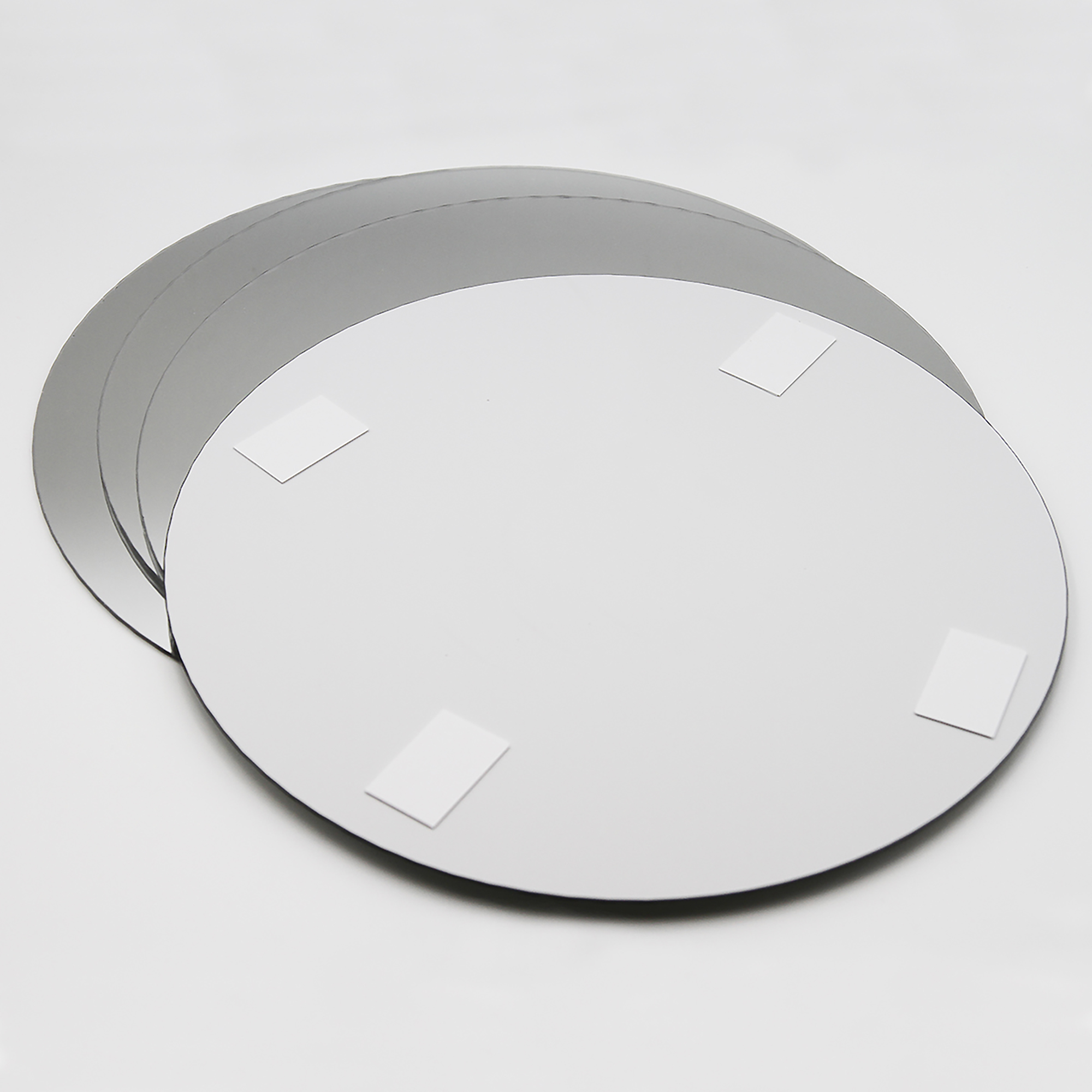 "Back of large round mirror showing four adhesive foam mounting pads, with three additional mirrors stacked behind"