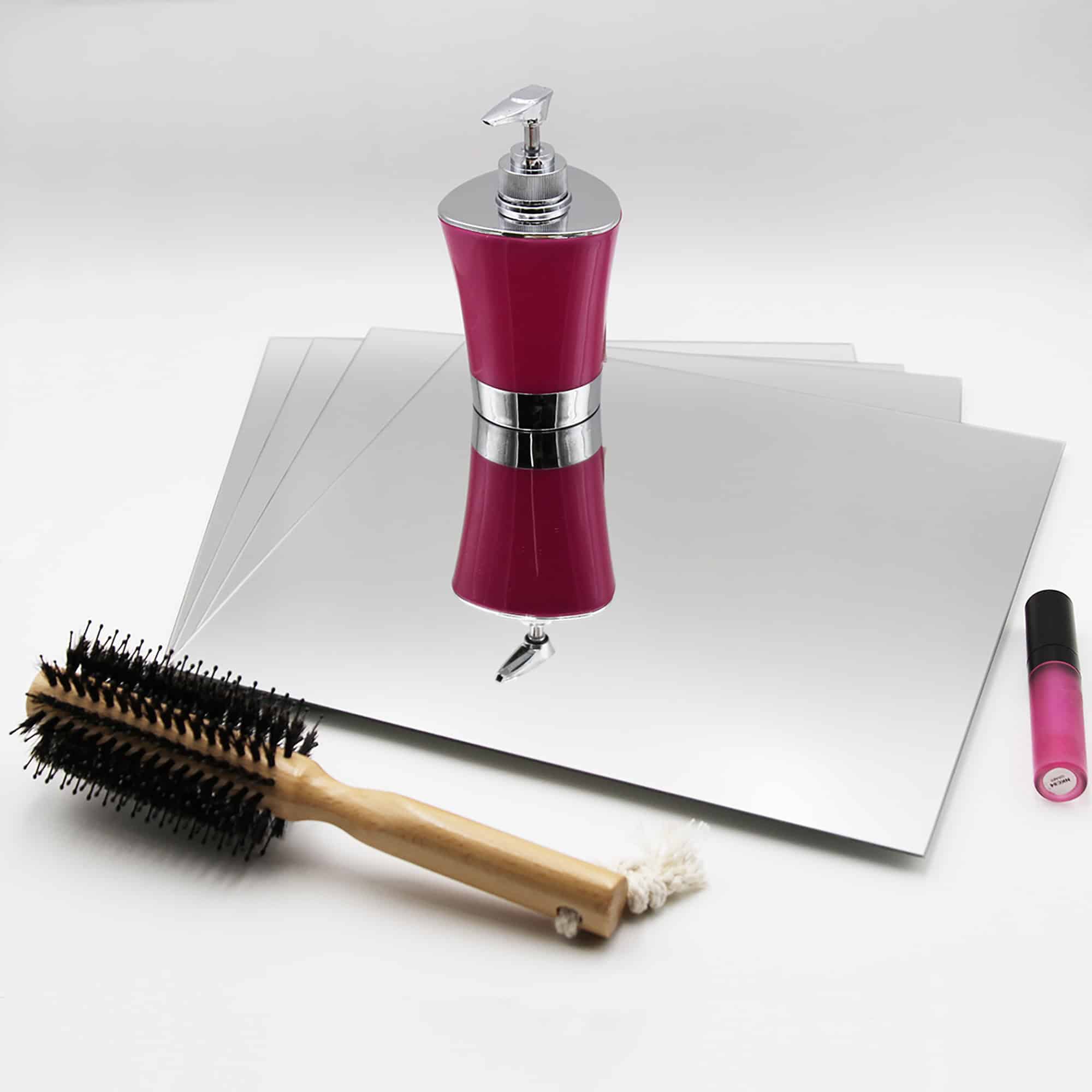 "Four stacked large square frameless mirrors lying flat beside a hairbrush and cosmetics"