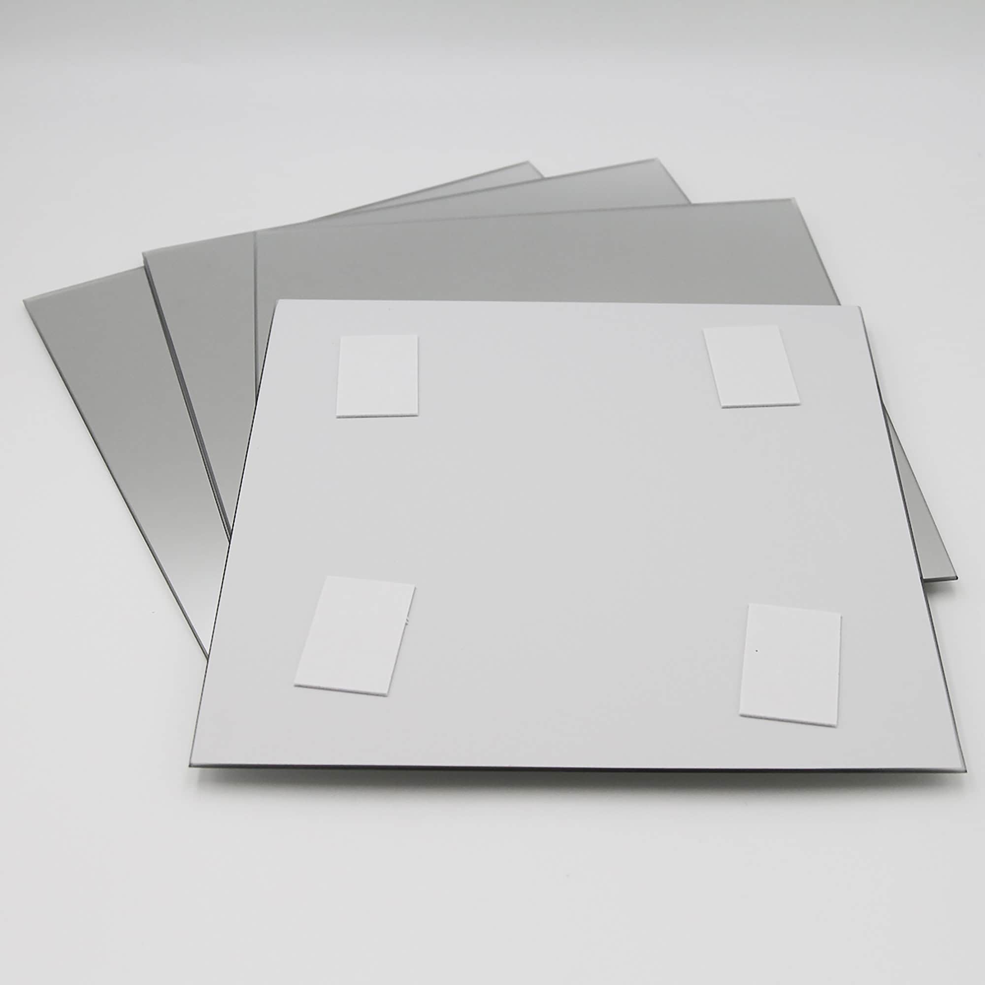 "Back of large square mirror showing four adhesive foam mounting pads, with three additional mirrors fanned behind"