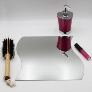 "Single large wave-shaped frameless mirror lying flat beside a hairbrush and cosmetics"