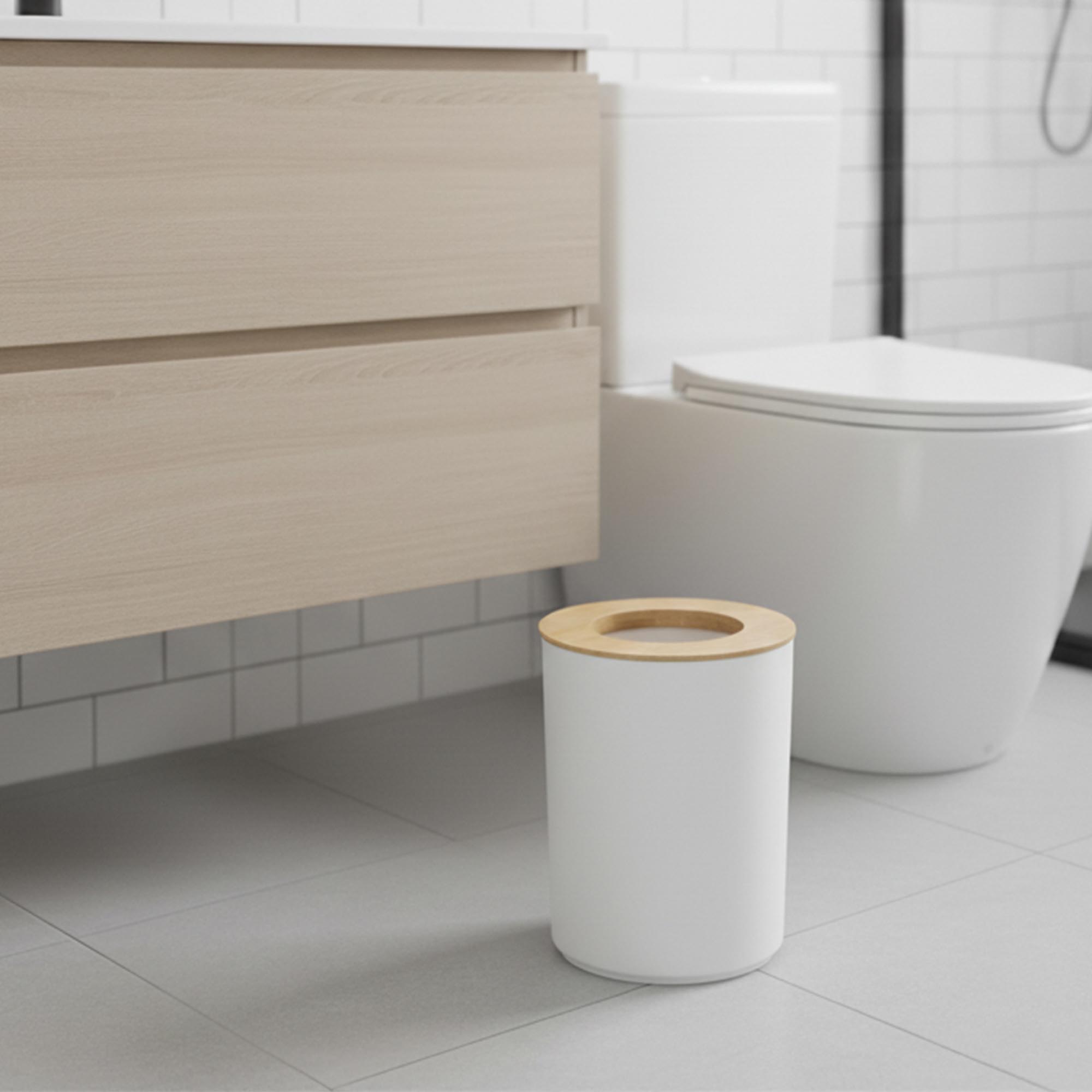 White bathroom trash can with bamboo top next to toilet brush