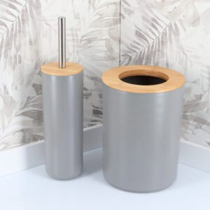 Gray toilet brush and matching waste bin with bamboo lids against tropical leaf wallpaper