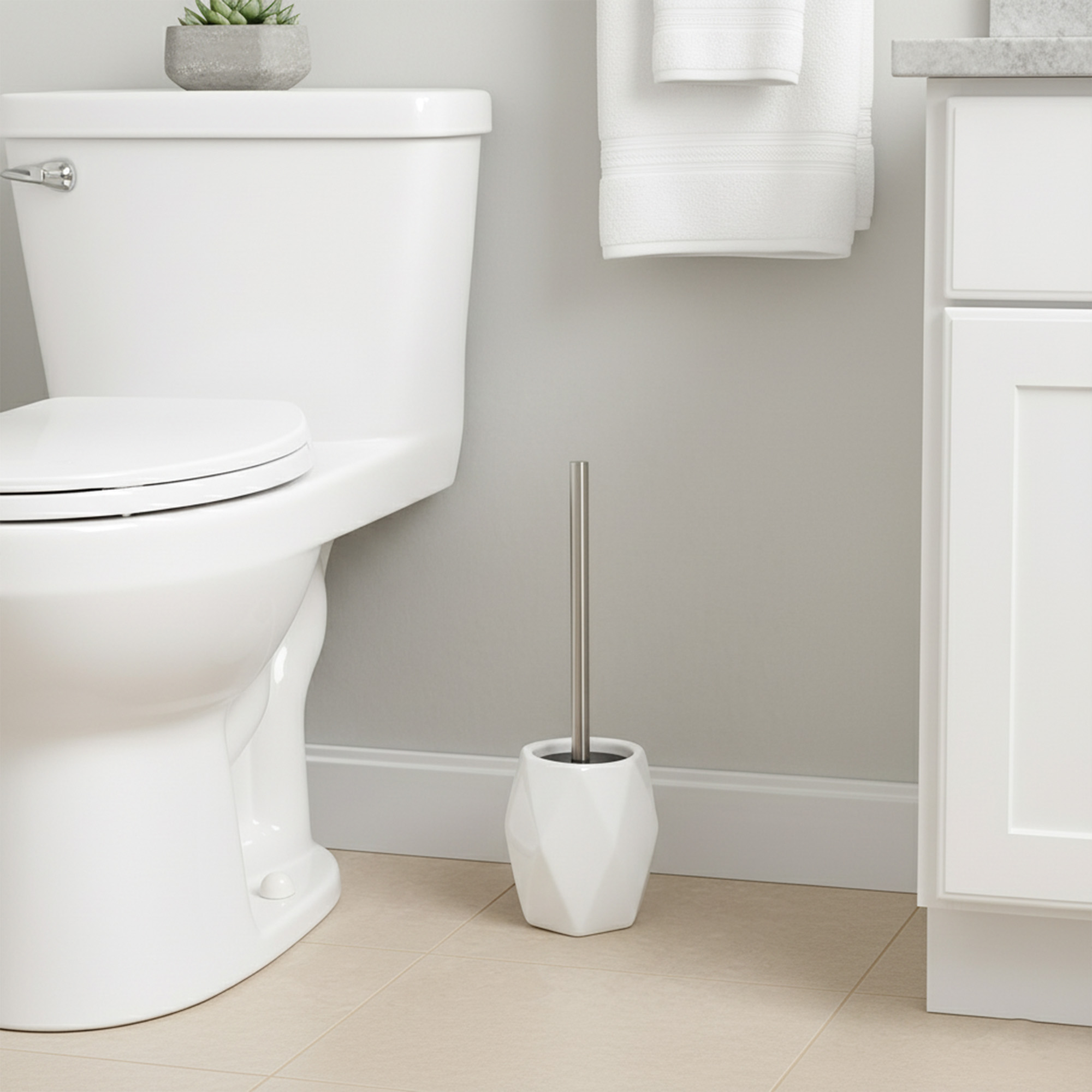White diamond-shaped stoneware toilet brush with stainless steel handle beside white toilet in modern bathroom
