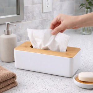 Hand pulling tissue from white rectangular tissue box with bamboo lid on bathroom counter