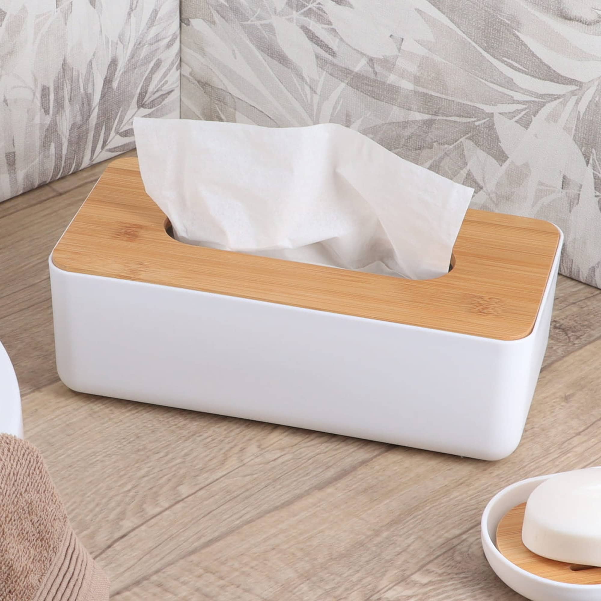 White tissue box with bamboo lid on wooden surface with neutral leaf pattern pillows