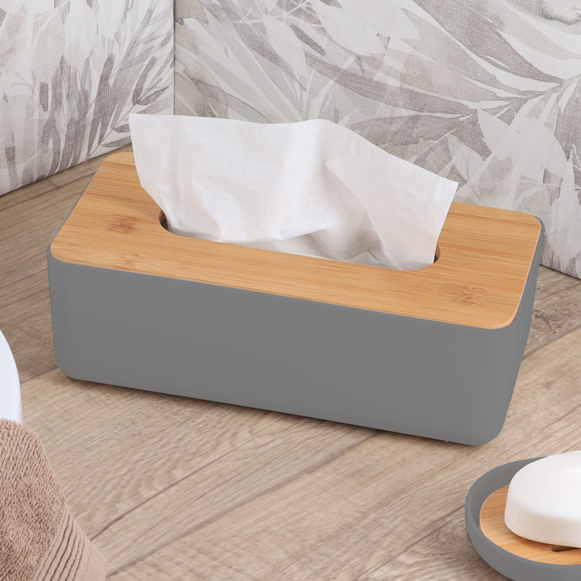 Gray tissue box with bamboo lid on wooden surface with neutral leaf pattern pillows