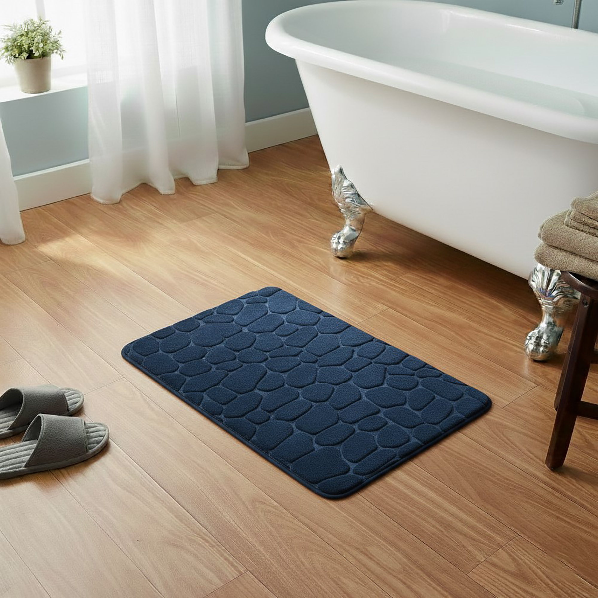 Navy blue memory foam bath mat with embossed pebble stone texture on wooden floor beside clawfoot tub