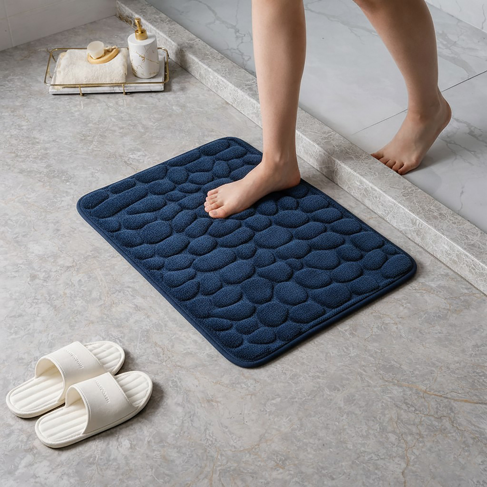 Person standing barefoot on a navy blue memory foam mat with pebble texture placed on a bathroom tile floor