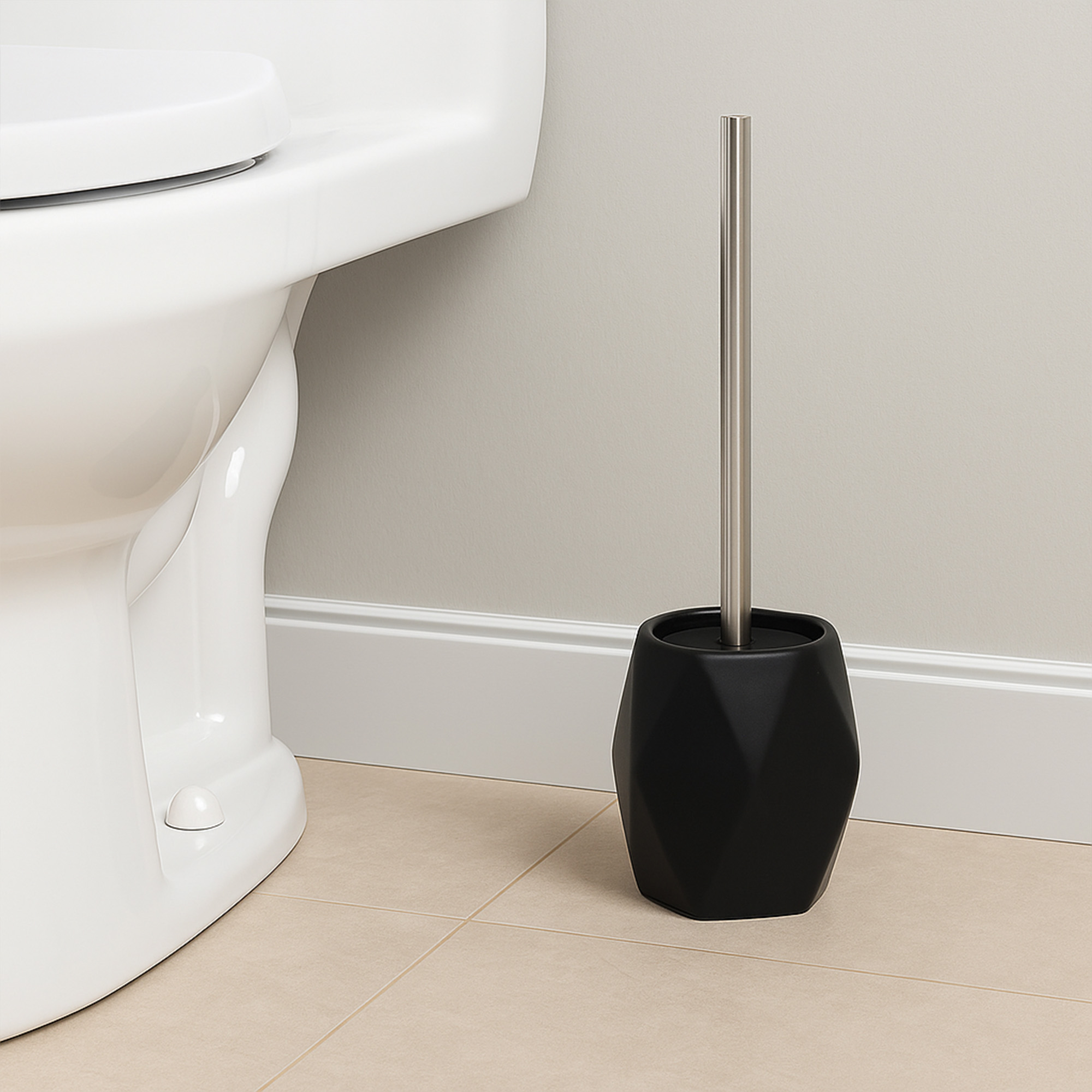 Black diamond-shaped stoneware toilet brush holder with stainless steel handle beside white toilet
