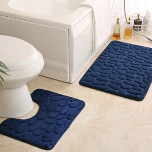 Navy blue pebble bath mat set featuring standard and contour shapes placed around white tub and toilet on beige tile floor