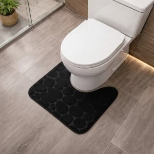 Black memory foam contour bath mat with pebble texture positioned around toilet base, angled view