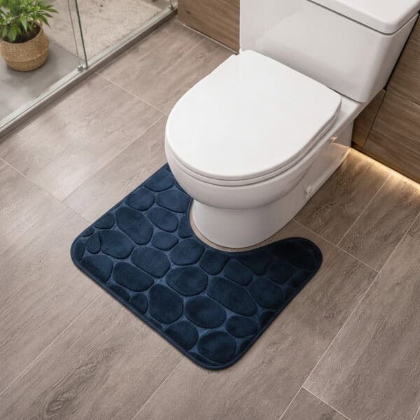 Navy blue memory foam contour bath mat with pebble texture positioned around toilet base, angled view