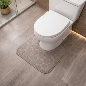 Taupe memory foam contour bath mat with pebble texture positioned around toilet base, angled view