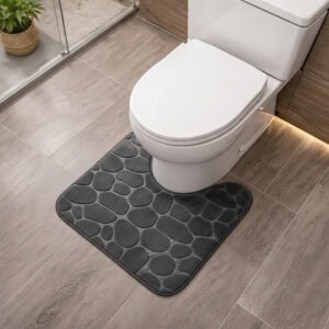 Dark gray memory foam contour bath mat with pebble texture positioned around toilet base, angled view