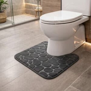 Dark gray pebble-embossed memory foam contour mat around toilet, side-angle view in modern bathroom