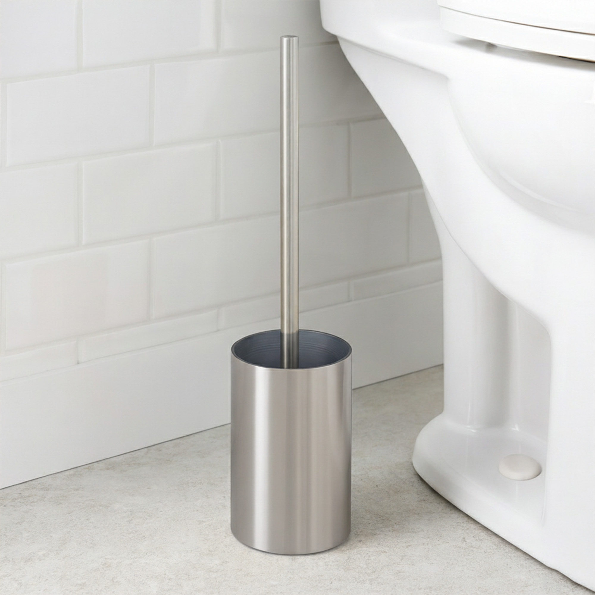 Brushed aluminum toilet brush holder beside white toilet against white subway tile