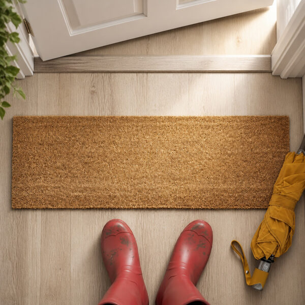 Top view of natural coir doormat at front door with red rain boots and yellow umbrella on light wood floor