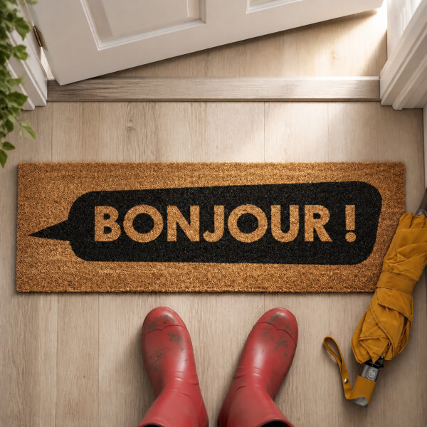 Bonjour long door mat on a light wood entry floor with red rain boots, top view of the natural coir doormat
