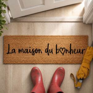 La Maison du Bonheur coir door mat on a wood entry floor with red rain boots and a yellow umbrella