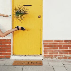 La maison du bonheur doormat in front of yellow door with person walking