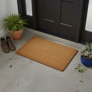Natural coir doormat 24x16 placed at black entry door with plants and boots
